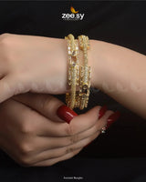 Aurumé Bangles, featuring a unique blend of elegance and modern craftsmanship. Designed with a golden polish, these exquisite kangans are adorned with dazzling diamond-cut stones and delicate stones, exuding a refined charm. The structured pattern and exquisite detailing enhance their luxurious appeal, making this kada an ideal choice for weddings, festive occasions, and special celebrations.