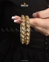 Champora Bangles exude a warm golden polish, blending champagne hues with intricate craftsmanship. Designed for timeless elegance, these exquisite kangan are adorned with shimmering American diamond stones, enhancing their refined sophistication. A perfect fusion of luxury and charm, they radiate grace and exclusivity, making this kada a stunning addition to any jewelry collection.