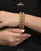 Champora Bangles exude a warm golden polish, blending champagne hues with intricate craftsmanship. Designed for timeless elegance, these exquisite kangan are adorned with shimmering American diamond stones, enhancing their refined sophistication. A perfect fusion of luxury and charm, they radiate grace and exclusivity, making this kada a stunning addition to any jewelry collection.