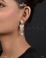 Flutura Earrings showcase a refined combination of pearls and diamond-cut stones, designed to exude sophistication and charm. Ethnic Festive Earrings are top features a luminous pearl, followed by an intricate floral motif adorned with shimmering stones, leading to a gracefully dangling pearl at the bottom.