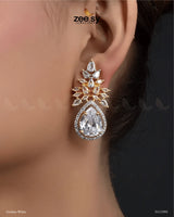 The Ivy Earrings showcase a mesmerizing combination of elegance and luxury, featuring dazzling crystal glass stones framed with sparkling American-cut diamond stones. These statement earrings boast a refined drop design with intricate detailing and a high-quality rhodium polish, adding a touch of sophistication to any outfit. Perfect for weddings, evening parties, and festive occasions.