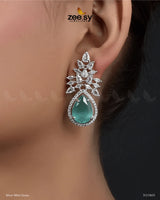 The Ivy Earrings showcase a mesmerizing combination of elegance and luxury, featuring dazzling crystal glass stones framed with sparkling American-cut diamond stones. These statement earrings boast a refined drop design with intricate detailing and a high-quality rhodium polish, adding a touch of sophistication to any outfit. Perfect for weddings, evening parties, and festive occasions.