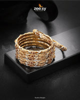 Kashira Bangles, feature an exquisite twisted design with intricate detailing and rhodium-polished accents. Adorned with delicate stone embellishments and fine craftsmanship, these bangles radiate elegance and charm. Perfect for festive occasions, weddings, and celebrations, they add a graceful touch to any ethnic attire.