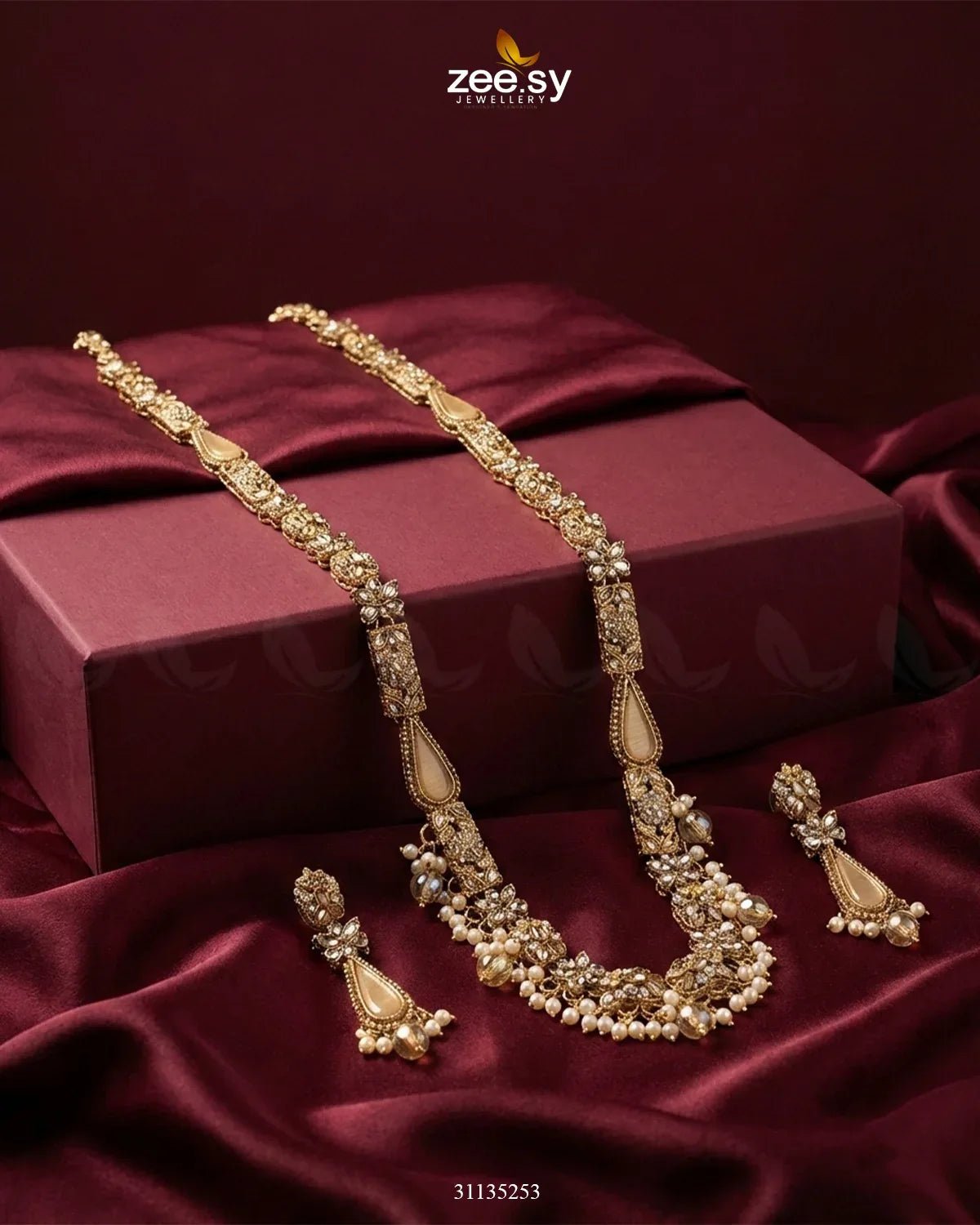 Gold necklace and earrings on a maroon fabric with 'zee sy' branding.