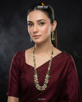 Woman wearing a maroon saree with green and gold jewelry against a dark background