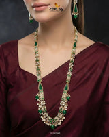 Woman wearing a green and gold necklace with matching earrings, against a dark background.