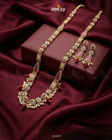 Ornate necklace and earrings set on a maroon fabric background with 'zee sy' branding.