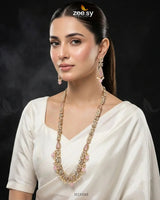 Woman wearing a long necklace with a dark background, featuring the Zee Sy brand.