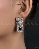 Vinca Earrings elegant statement earrings feature a captivating design adorned with dazzling American-cut diamond stones and shimmering crystal glass stones. The intricate floral motif at the top adds a delicate touch, leading to a stunning rectangular crystal centerpiece surrounded by a halo of sparkling accents. Available in multiple variants, these Danglers these earrings offer versatility and luxury to complement any outfit.