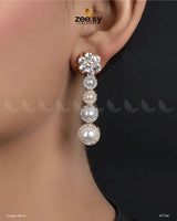 Vyom Earrings embody elegance and sophistication with their luxurious design. Featuring a dazzling arrangement of&nbsp;American-cut diamond stones, Vintage Pearl Earrings are adorned with luminous pearls in a cascading pattern, creating a graceful and timeless look. The refined setting is complemented by a golden or silver polish, adding a radiant finish that enhances their beauty.