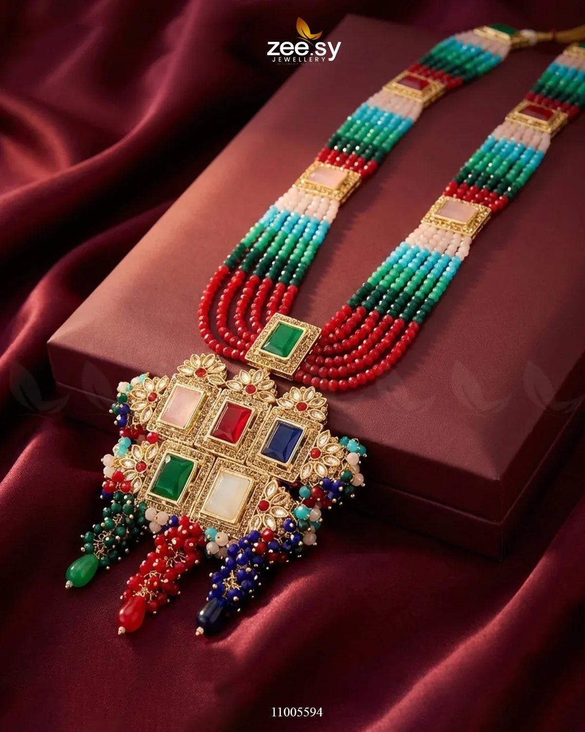 Colorful beaded necklace with gold and gemstone details on a red fabric background, featuring the brand 'zee sy'.