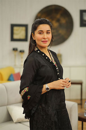 Woman wearing black traditional outfit with subtle jewelry, standing indoors in a modern living space